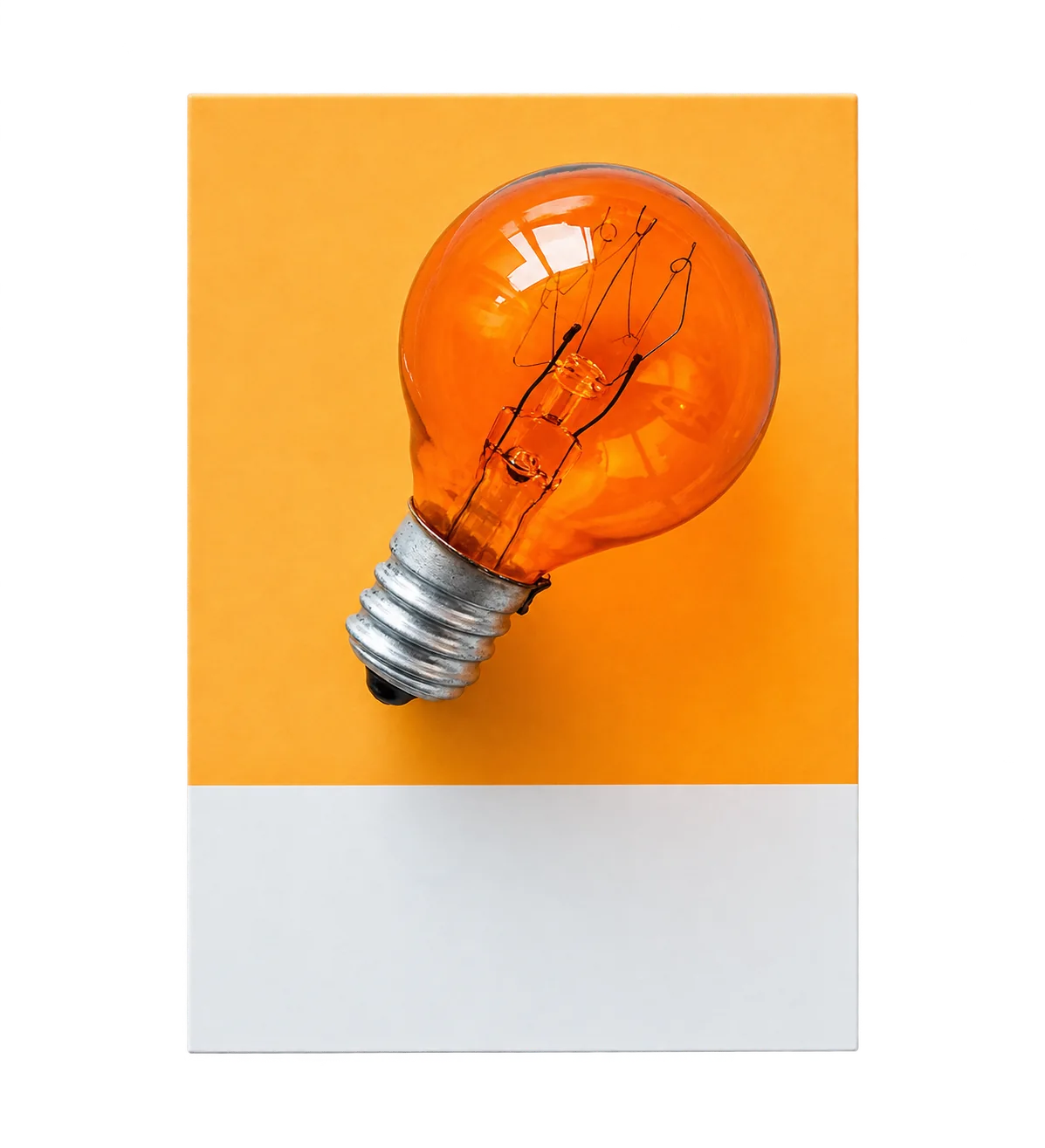 Une ampoule orange à filament posée sur une carte orange et blanche, sur un fond turquoise uni.